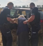 policjanci pomagają starszej kobiecie wsiąść do radiowozu