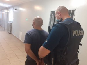 Na korytarzu aresztu umundurowany policjant zakłada zatrzymanemu kajdanki