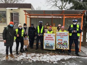 Dzieci wspólnie z policjantami przeprowadzają kontrole drogowe kierowców i wręczają woreczki  z ziemia  lub uśmiechnięte zawieszki, dzieci trzymaję w rękach plakat akcji