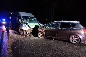 na zdjęciu widoczne są dwa uszkodzone pojazdy - osobowy i bus, stojące do siebie przodem na jezdni; jest noc