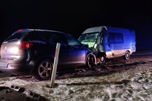 na zdjęciu widoczne są dwa uszkodzone pojazdy - bus i osobowy; pojazdy stoją na poboczu jezdni; jest noc; na pierwszym planie - łupek hektometrowy