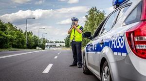 na poboczu drogi przed radiowozem stoi umundurowany policjant w kamizelce odblaskowej