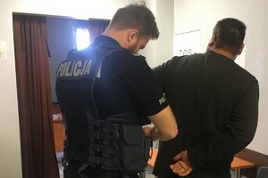 w areszcie policjant  zakłada zatrzymanemu u kajdanki na ręce trzymane z tyłu