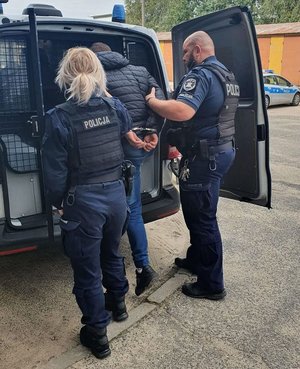 zatrzymany prowadzony przez dwóch umundurowanych policjantów wsiada do radiowozu