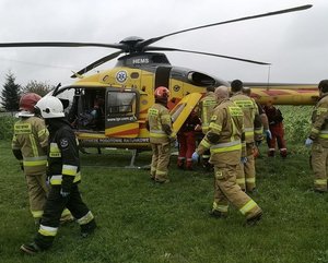 W tle śmigłowiec z lotniczego pogotowia ratunkowego, funkcjonariusze z państwowej straży pożarnej oraz ratownicy medyczni.