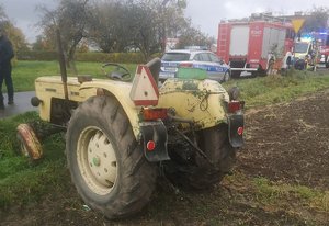Ciągnik rolniczy stojący na polu, w tle widać pojazdy policji, straży pożarnej oraz pogotowia ratunkowego.