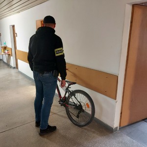 na korytarzu komendy policjant z opaska na ramieniu  z napisem POLICJA stoi przy odzyskanym z kradzieży rowerze