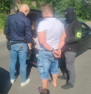 policjant przeszukuje bagażnik samochodu obok samochodu dwóch policjantów oraz zatrzymany mężczyzna który ma założony kajdanki na ręce trzymane z tyłu