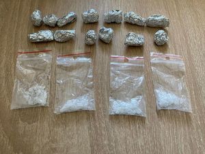 Na stoliku leżą woreczki foliowe z białą krystaliczną substancją oraz zawiniątka ze srebrnej folii.