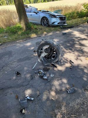 Miejsce wypadku drogowego, rozbity samochód srebrny który uderzył w  drzewo, porozrzucane elementy karoserii.