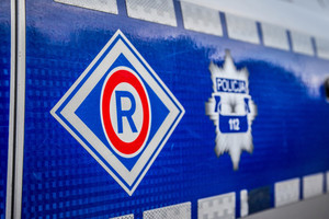 Bok policyjnego radiowozu, napis policja oraz litera R w otoczce  kształcie rombu koloru czerwonego.