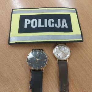 Na stole leżą dwa zegarki, obok opaska z napisem POLICJA.