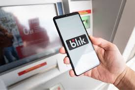 Monitor bankomatu, przed nim telefon trzymany  w dłoni, na którego wyświetlaczu widoczny jest napis BLIK.