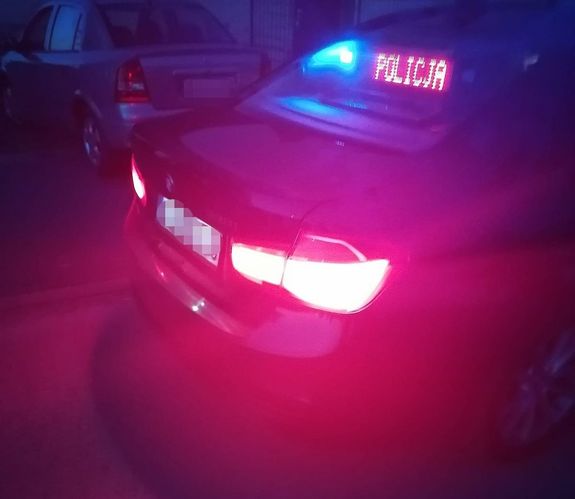 Tył policyjnego nieoznakowanego radiowozu z podświetlonym napisem POLICJA, obok stoi opel koloru szarego.