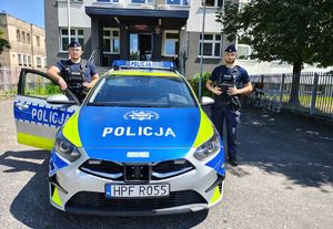 Przed budynkiem komendy z po obu stronach radiowozu oznakowanego stoją umundurowani policjanci.