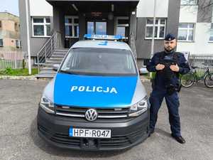 Przed budynkiem komendy z przy radiowozie oznakowanym stoi umundurowany policjant.