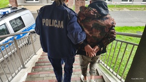 Umundurowana policjantka prowadzi zatrzymanego po schodach, ma on założone kajdanki.