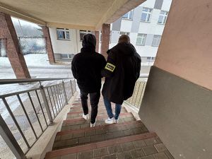 Po schodach policyjnego aresztu policjant prowadzi zatrzymanego mężczyznę.