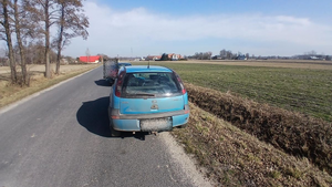 Z prawej strony drogi  stoi samochód osobowy koloru niebieskiego, przed nim stoi samochód osobowy koloru ciemnego.