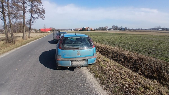 Z prawej strony drogi stoi samochód osobowy koloru niebieskiego, przed nim stoi samochód osobowy koloru ciemnego.