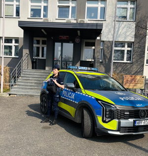 Przed budynkiem komendy na tle radiowozu stoi umundurowana policjantka.