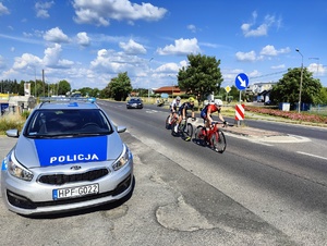 Trzech kolarzy ucieka przed peletonem. Na skrzyżowaniu stoi radiowóz, zabezpieczający wjazd na trasę wyścigu.