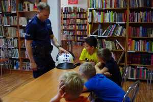 Policjant pokazuje dzieciom kask przeciwuderzeniowy.