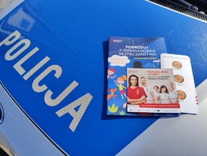 Na masce policyjnego radiowozu leża ulotki informujące dotyczące kampanii &quot;bezpieczny przejazd&quot;.