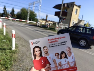 Ulotka bezpieczny przejazd. Posłuchaj głosu rozsądku. Uważaj na przejeździe kolejowo-drogowym. W tle zamknięty przejazd kolejowy.