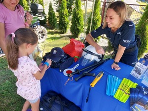 Policjantka uśmiecha się do dziewczynki, która otrzymała własnie opaskę odblaskową.