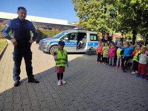 Policjant pozuje wraz z dziewczynką w czapce policyjnej do zdjęcia.