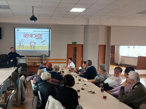 Policjanci dają wykład o bezpieczeństwie seniorów. Na ekranie projektora wyświetla się grafika z tekstem &quot;seniorze nie daj się!&quot;.