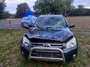 Uszkodzony przód samochodu marki Toyota. W tle widać policyjny radiowóz.