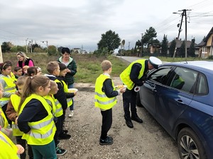 Policjant rozmawia z kierującym, za policjantem stoją dzieci.