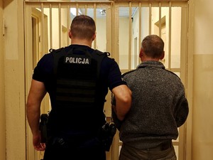 Policjant trzyma pod rękę zatrzymanego mężczyznę.