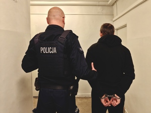 Policjant trzyma pod rękę zatrzymanego mężczyznę.