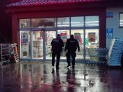dwóch umundurowanych policjantów stojących tyłem przed jednym ze sklepów.