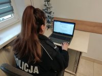 policjanta w mundurze siedzi przy biurku na którym jest laptop.