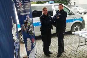 Zdjęcie przedstawia dwie umundurowane policjantki stojące na tle radiowozu przy stoisku promocyjnym Komendy Powiatowej Policji w Łęczycy.