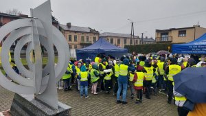 Policjanci, uczestnicy wydarzenia ubrani w kamizelki odblaskowe. W tle budynki a na pierwszym planie figura geograficznego środka Polski.