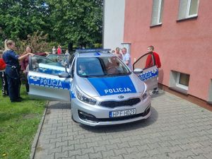 Policjantka wraz z dziećmi stoi obok radiowozu.