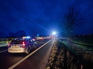 Radiowóz z włączonymi światłami na jezdni oraz policjanci pracujący na miejscu wypadku.