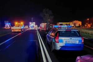 Miejsce wypadku, policyjny radiowóz stojący na sygnałach, w tle pojazdy innych służb ratunkowych.