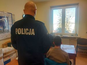 Policjant stoi tyłem, a obok podejrzany podczas przesłuchania.