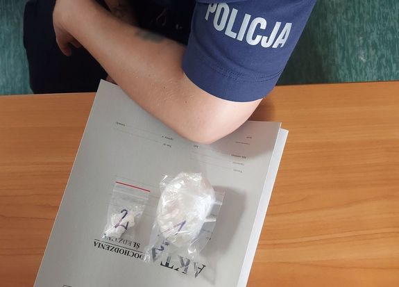 Porcja zabezpieczonych narkotyków leży na aktach sprawy obok ramię policjanta.