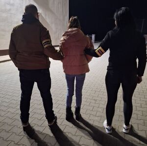 Policjanci z zatrzymaną stoją tyłem.