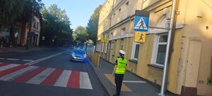 Policjant stojący przy radiowozie w rejonie przejścia dla pieszych.