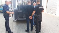 Dwóch policjantów z zatrzymanym przed radiowozem.