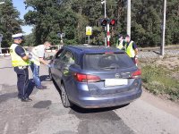 Policjanci wspólnie z pracownikami PKP , samochód stoi przed przejazdem kolejowym. Pracownik PKP rozmawia z kierowcą