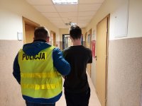 korytarz w Komendzie Powiatowej Policji w Kutnie, policjant w kamizelce odblaskowej z napisem POLICJA prowadzi zatrzymanego